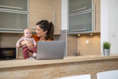 Bilgisayarda bebeği olan bir iş kadını anne. Mutfakta dizüstü bilgisayar kullanan bir anne..