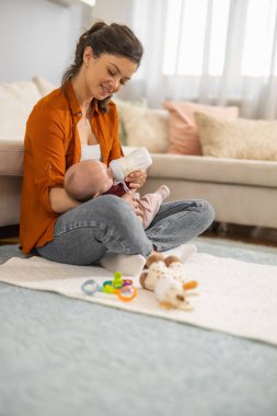 Bir kadın yenidoğanı sütle besler. Güzel bir anne evde yerde otururken bebeği mama ile besler..