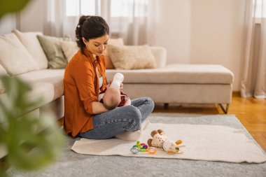 Bir kadın yenidoğanı sütle besler. Güzel bir anne evde yerde otururken bebeği mama ile besler..