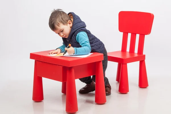 Schattige kleine jongen tekening, rode tafel en stoel, op witte achtergrond. Jeugd onderwijs concept — Stockfoto