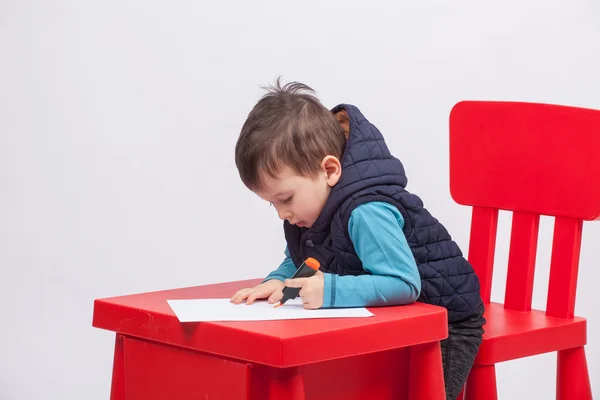 Bonito desenho menino, mesa vermelha e cadeira. Conceito de educação infantil — Fotografia de Stock