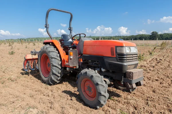 Kleiner roter Traktor mit Pflug im Feld. — Stockfoto