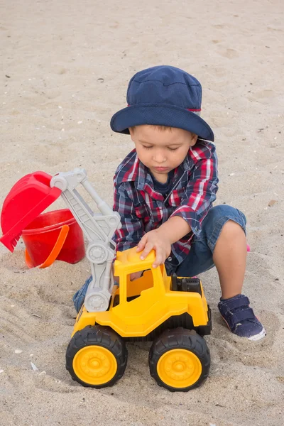 Милый мальчик играет с экскаватором на пляже — стоковое фото