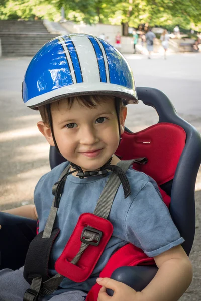 Un niño sonriendo en la bicicleta del asiento. El chico tiene casco de ciclista. Protección en la bicicleta . — Foto de Stock