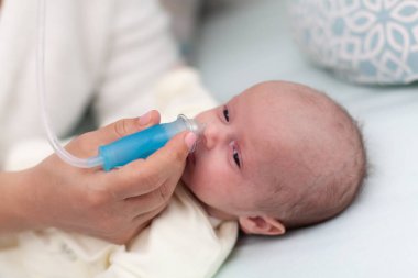 Anne aspiratörle temizlik yapıyor, yeni doğmuş bebeğin burnunu tıbbî aletle temizliyor. Bebeğinin burnunu temizlemek için burnunu pompalayan şefkatli bir anne..