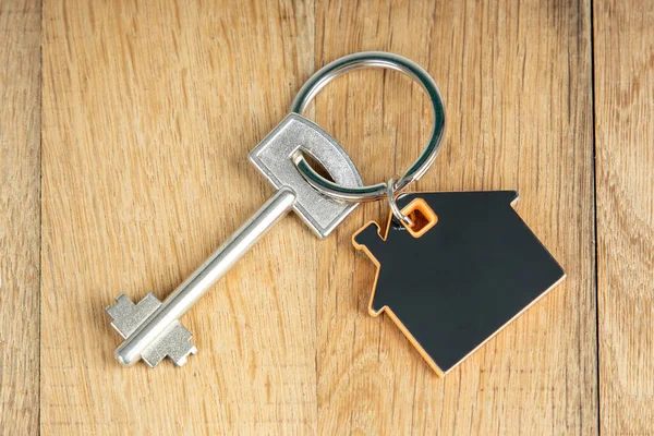 Close up home shaped keychain with key on wooden background. Mortgage, investment, real estate, property and new home concept