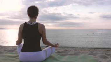 Plajda nilüfer çiçeği pozu veren kadın. Güneşin doğuşunda deniz kenarında meditasyon.