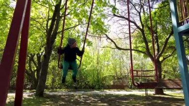 Küçük çocuk dışarıda oyun alanında eğleniyor. Sallanıyor salıncakta. 