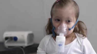 Astım spreyi maskesi takmış şirin bir kız. Evde solunum prosedürü uygulanıyor. Çocuk nebulizörle solunum terapisi görüyor..