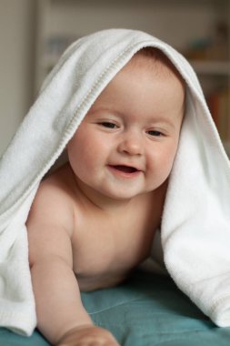 Küçük bebek gülümsüyor, gülüyor. Beyaz havlunun üzerinde tatlı bir bebek yatıyor..