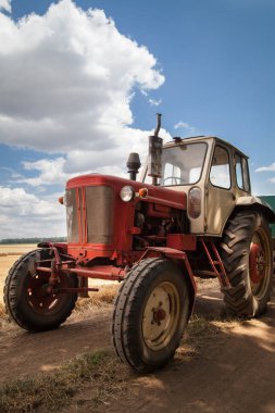 Yaşlı traktör sahada, bulutlu bir gökyüzüne karşı.