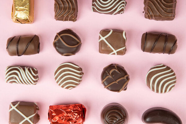 top view of various chocolate pralines on pink background. Collection chocolates candy. Assorted chocolates on pink