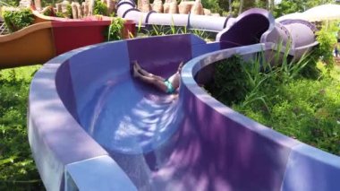 Çocuk yaz tatilinde su parkında kayıyor. Mutlu çocuk su kaydırağından kayıyor.