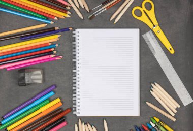 Tahtada renkli okul malzemeleri var. Kalemleri, kalemleri ve pastel boyaları olan boş bir not defteri. Okul konseptine dönelim..