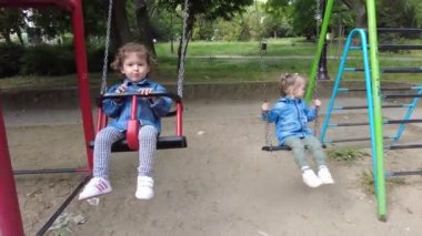 İki küçük kız, oyun alanında oynuyorlar. Çift yumurta ikizi kardeşler, salıncakta sallanıyorlar