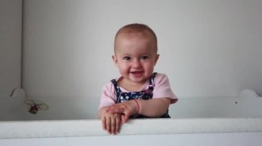 Sevimli bebek gülüyor ve eğleniyor, beşiğinde duruyor. Mutlu bebek. Bebek duyguları. Bebek gülümsemesi.