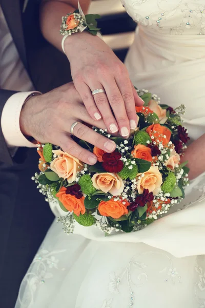 Руки жениха и невесты с обручальными кольцами и букетом цветов — стоковое фото