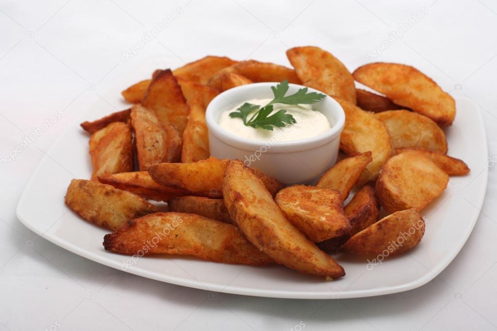 Fried potato wedges with white sauce on white plate Stock Photo by