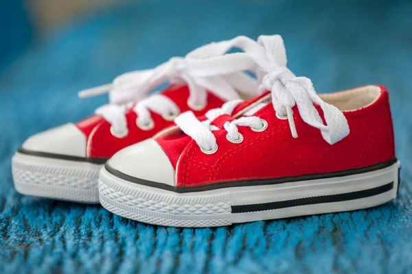 Zapatillas de deporte de bebé rojas sobre fondo azul madera — Foto de Stock