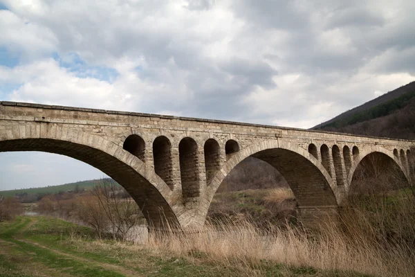 Старый каменный мост среднего возраста в Болгарии, против облачного неба — стоковое фото