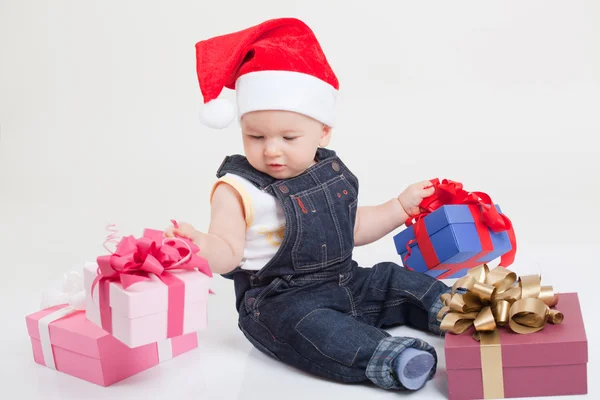 Niedliches Baby mit Weihnachtsmütze sitzt mit Geschenken Stockbild