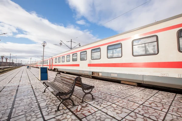 Plataforma com banco e trem na estação de trem — Fotografia de Stock