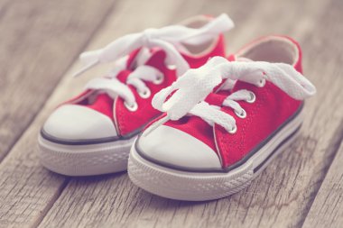 Red baby sneakers on wooden background. Vintage style image clipart