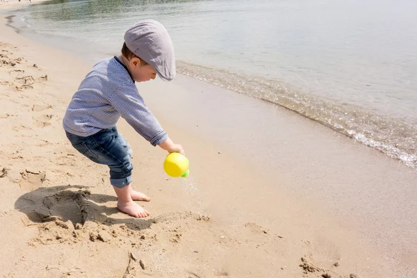Cute little boy playing with watering can on the beach