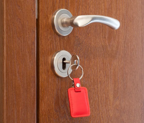 Handle pintu dengan kunci disisipkan dalam lubang kunci dengan pemegang kunci merah — Stok Foto