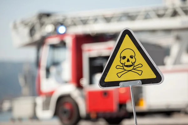 Tecken på fara med dödskalle, brandbil på bakgrund — Stockfoto
