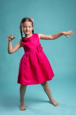 Açık pembe elbiseli, dans eden ve poz veren çıplak ayaklı bir kız. Mutlu, enerjik bir çocuğun tam boy stüdyo portresi 