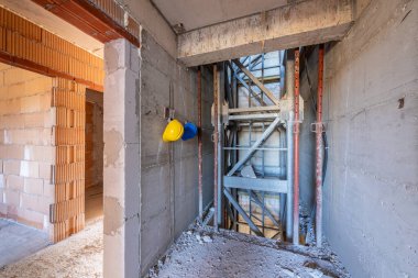 İnşaat halindeki bir binanın içinde. Bitmemiş asansör boşluğu, işlenmemiş beton ve tuğla duvarlar