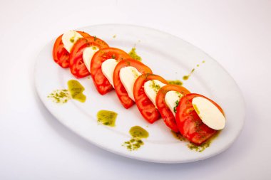 Taze domates, mozzarella ve pesto soslu gurme Caprese salatası. Beyaz bir tabakta servis edilen sağlıklı bir Akdeniz aperatifi.