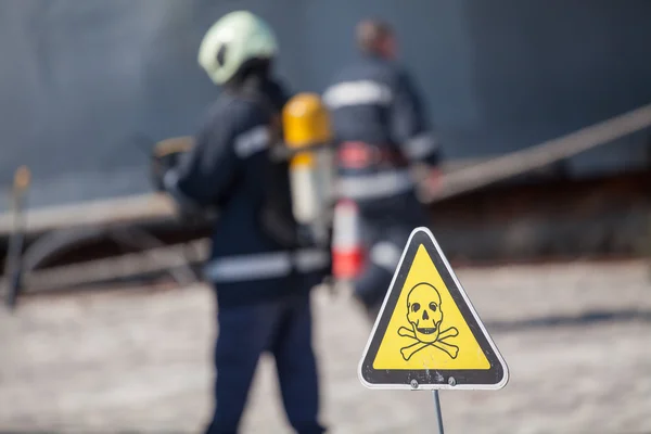 Danger sign with skull and crossbones, firefighters on background — Stock Photo, Image