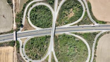 Simetrik yonca yaprağı otoyol kavşağının yukarıdan aşağı görüntüsü. Yol ağındaki otomobiller kırsal bir alanda ulaşımı ve lojistiği gösteriyor, bağlantı ve altyapıyı sembolize ediyor.