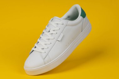 Sarı arka planda beyaz spor ayakkabı. Günlük moda, spor giyim ve sokak kıyafetleri için modern ve şık ayakkabılar..