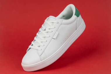 Kırmızı arka planda beyaz spor ayakkabı. Günlük moda, spor giyim ve sokak kıyafetleri için modern ve şık ayakkabılar..