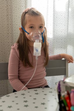 Astım spreyi maskeli küçük bir kız. Evde solunum prosedürü uygulanıyor. Çocuk nebulizörle solunum terapisi görüyor..