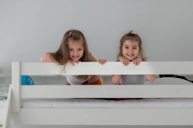 Küçük mutlu kızlar ranzada oynuyor. Çocukluk eğlencesi, kardeş bağı ve evdeki neşeli anlar. Şirin Kız Kardeş Gülümsüyor