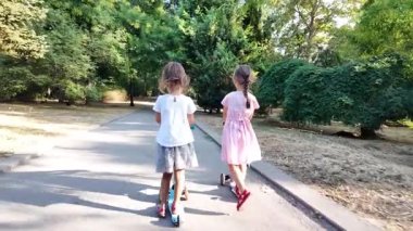 Parkta scooter süren iki kız. Çocuklar dışarıda mobiletlerle eğleniyor..