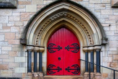 Tarihi bir taş binada süslü siyah işlemeli demir detaylarıyla Gotik tarzı kemerli kırmızı kapı. Simetrik mimari ve karmaşık tasarım çarpıcı, zamansız bir giriş yaratır..