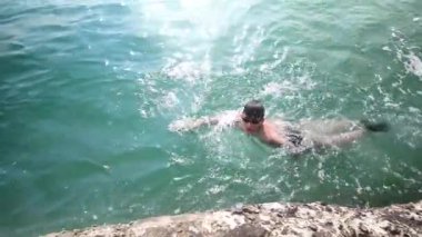 Açık Turkuaz Deniz 'de Yüzen Genç Adam Rocky Shore yakınında, Açık Hava Macerası. Sağlıklı Yaşam Tarzı ve Tatil Konsepti.