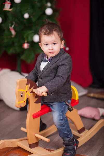 Small boy ride wooden rocking horse in front of christmas tree — Stock Photo, Image