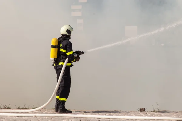 Bombero en traje protector funciona con manguera de agua. Luchando por un ataque de fuego —  Fotos de Stock