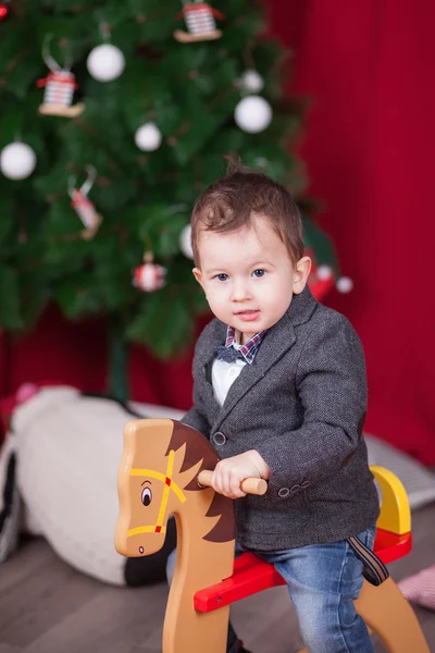小さな男の子がクリスマス ツリーの前で木製ロッキング馬に乗る — ストック写真
