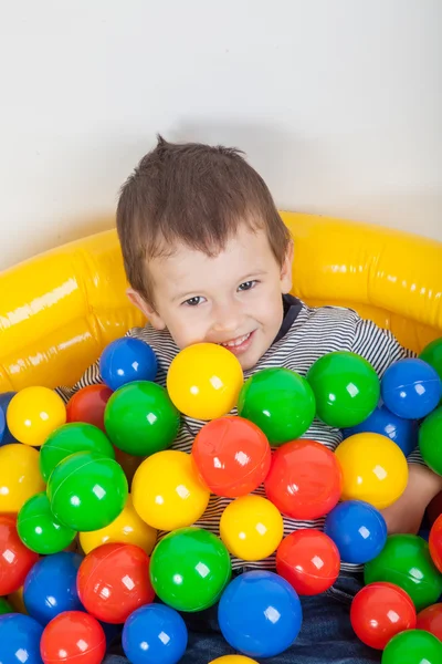 Piccolo ragazzo sorridente che gioca sdraiato nel parco giochi colorato palle — Foto Stock