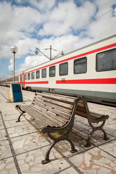 Plataforma con banco y tren en la estación de tren — Foto de Stock