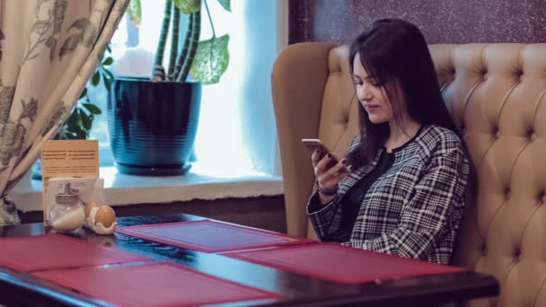 Beautiful girl with the phone. Woman using app on smartphone in cafe. Texting on mobile phone. — Stock Video