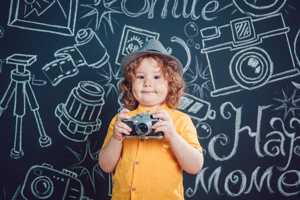 Niño pequeño con una cámara de pie sobre un fondo de paredes negras con palabras —  Fotos de Stock