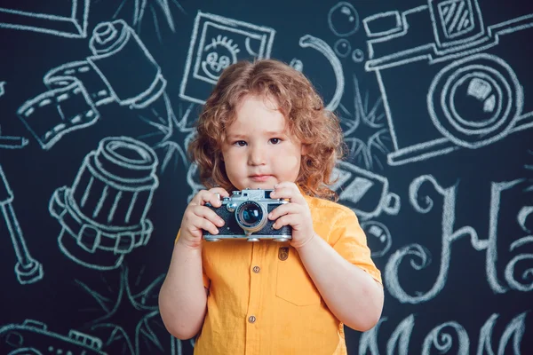 Маленький хлопчик з камерою, що стоїть на тлі чорних стін зі словами — стокове фото
